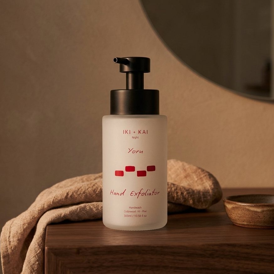 Hand exfoliator bottle on a wooden surface with a towel and bowl in the background